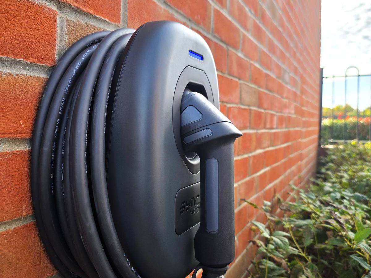 A Sync Energy home EV charger with tethered cable installed on a brick wall by NSS Electrics